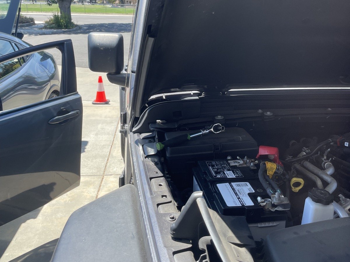 Battery under an open hood, with the terminals and label visible