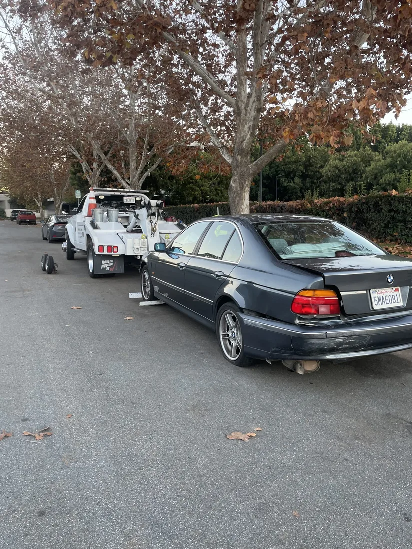 A dark BMW sedan parked on a tree-lined street beside a white service truck.