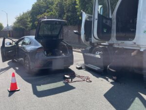 Jump start on site: a car and a semi-truck with doors open, a cone and jumper cables on the pavement