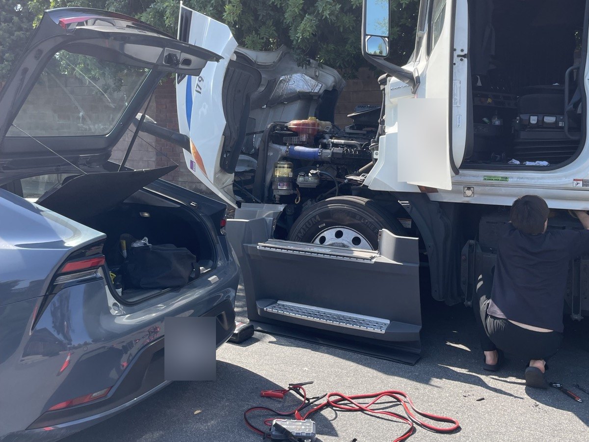 A semi-truck with its cab open and jumper cables on the ground beside it during a jump start